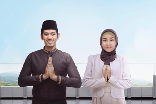 Asian muslim man and woman with traditional dress praying together against blue sky background