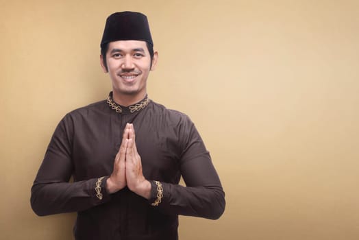 Handsome asian muslim man wearing traditional dress praying against brown background