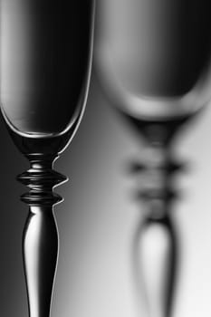 Detailed view of the middle parts of two champagne glasses brightness running background  monochrome. The focus is on the front glass.
