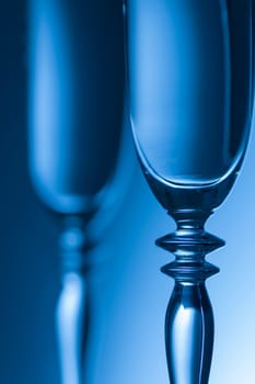 Detailed view of the middle parts of two champagne glasses Brightness running background shaded blue. The focus is on the front glass.