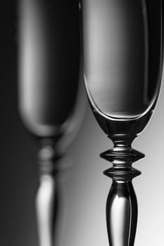 Detailed view of the middle parts of two champagne glasses brightness running background  monochrome. The focus is on the front glass.
