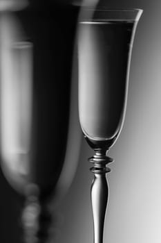 Detailed view of the tops of two champagne glasses against a background with brightness gradient  monochrome. The focus is on the rear glass.