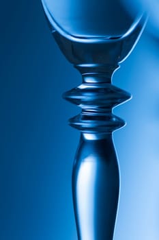 Detailed view of the middle part of a champagne glass with brightness gradient in the background  toned blue.