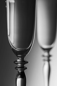 Detailed view of the middle parts of two champagne glasses brightness running background  monochrome. The focus is on the front glass.