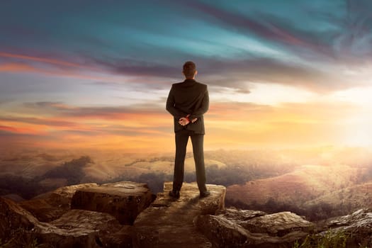 Back view of asian businessman on the top of the hill looking wonderful scenery in mountains during sunset