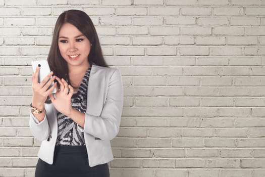 Smiling asian business woman using a mobile phone with white wall background