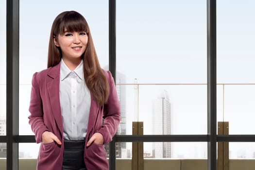 Smiling asian business woman standing in front of windows in an office