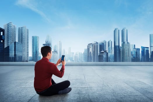 Portrait of asian businessman using a smartphone while sitting on terrace against cityscape background