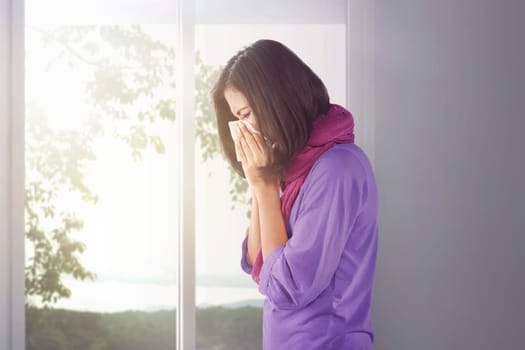 Sick asian woman holding a tissue in her nose at home