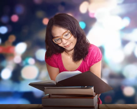 Charming asian woman sitting by wooden table and reading book against blurred background