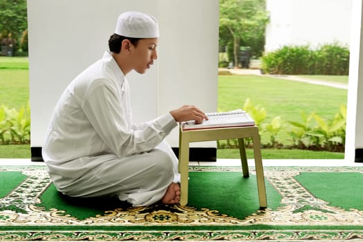 Side view of asian muslim man reading holy book koran on the mosque