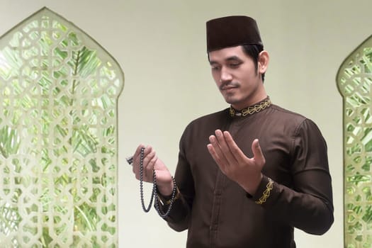 Young asian muslim man praying with prayer beads in the mosque