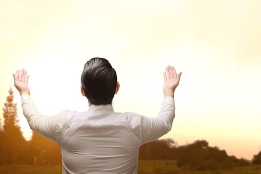 Back view of asian muslim man raising hand and praying during sunset