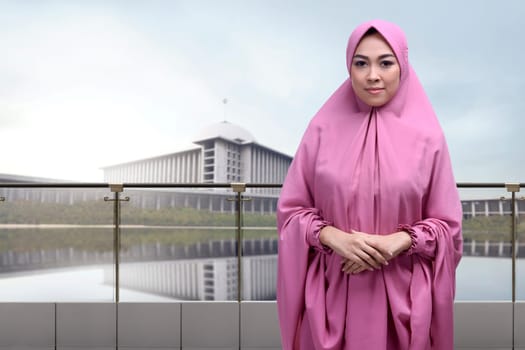 Religious asian muslim woman wearing veil with clasping hand standing against mosque background