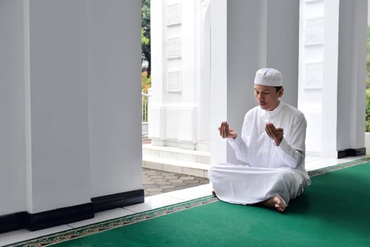 Handsome asian muslim man raising hand and praying on the mosque