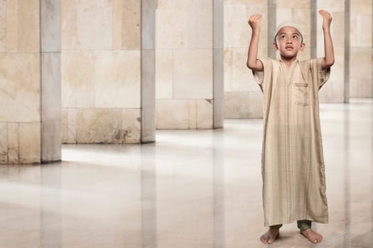 Little asian muslim boy raising hand and praying on the mosque