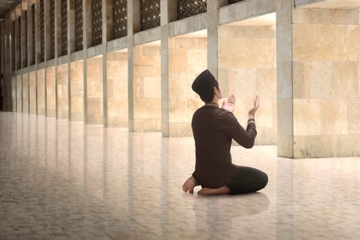Religious asian muslim man raising hand and praying on the mosque