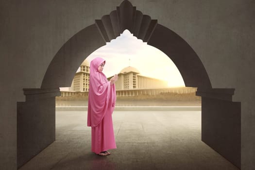 Beautiful asian muslim female wearing veil raising hand and praying with mosque background