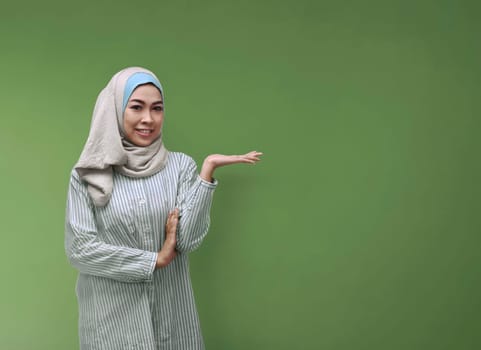 Happy asian muslim woman in veil showing blank area over green background for copyspace