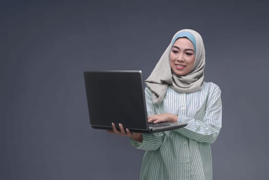 Portrit of asian muslim woman with hijab typing on laptop over dark background