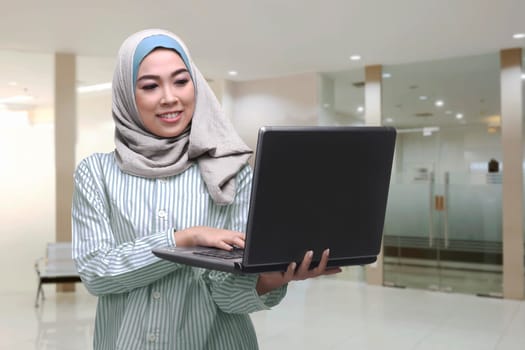 Young asian muslim woman using laptop while standing in the office room
