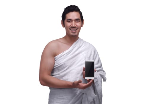 Young asian muslim man wearing ihram dress holding phone isolated over white background