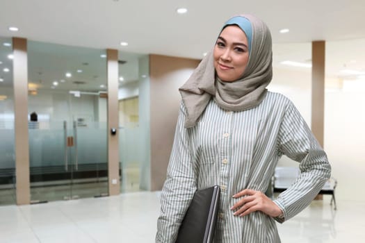 Beautiful asian muslim woman with hand at waist holding laptop on the office