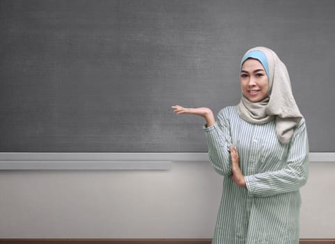 Beautiful asian muslim woman wearing hijab showing copyspace area on the blackboard