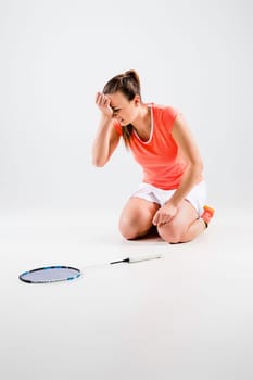 Young woman playing badminton over white studio background. A symbol of defeat and failure