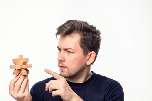 Attractive 25 year old business man looking confused and surprised at wooden puzzle on white studio background.