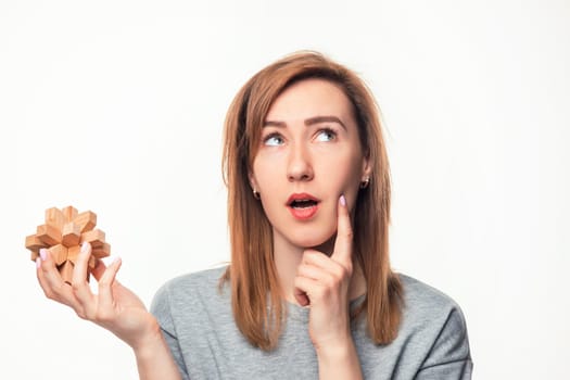 Attractive 24 year old business woman looking confused and surprised at camera with wooden puzzle on white studio background.