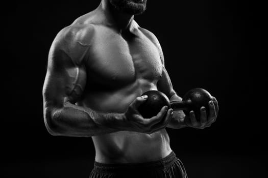 The colorless image of torso of attractive male body builder with weight on black studio background.