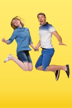 Portrait of a young couple jumping against yellow studio background
