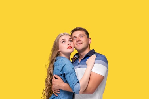 Portrait of a young couple standing against yellow studio background and looking up