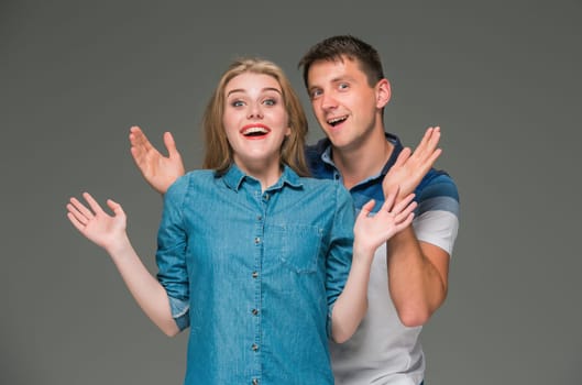 Portrait of a young surprised couple standing against gray studio background