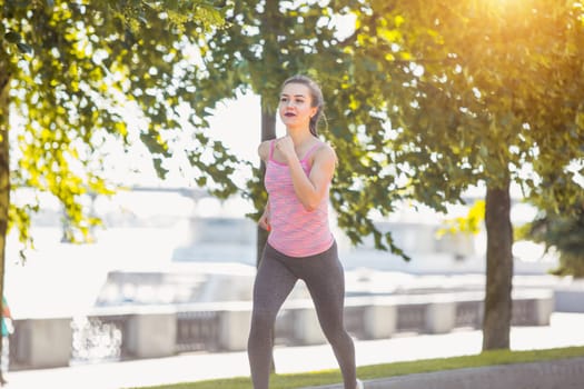 Pretty sporty woman jogging at park in sunrise light at morning