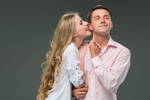 Portrait of a young couple standing against gray studio background. woman whispering in man ear