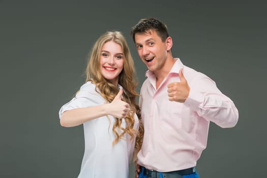 Portrait of a young couple standing against gray studio background with sign ok