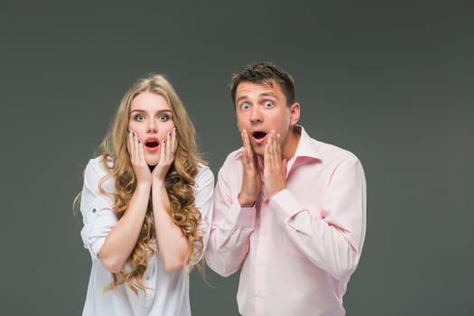 Portrait of a young surprised couple standing against gray studio background