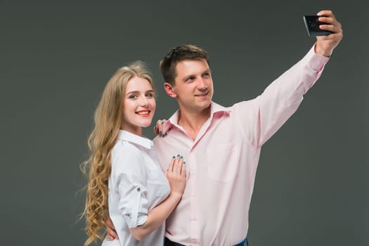 Portrait of a young couple standing against gray studio background and making selfies