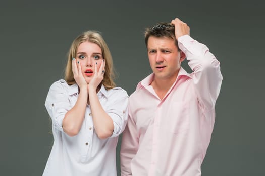 The young couple with different emotions during conflict on gray background