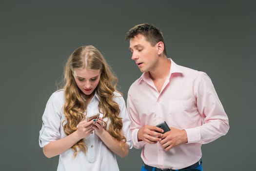 Business concept. The two young colleagues holding mobile phones and speaking on gray studio background