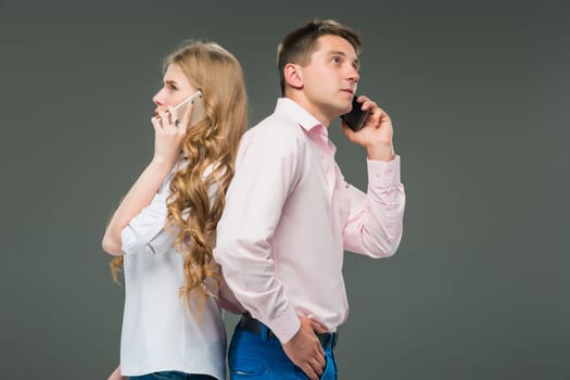 Business concept. The two young colleagues holding mobile phones and speaking on gray studio background