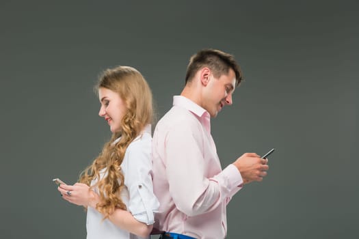 Business concept. The two young colleagues holding mobile phones and speaking on gray studio background