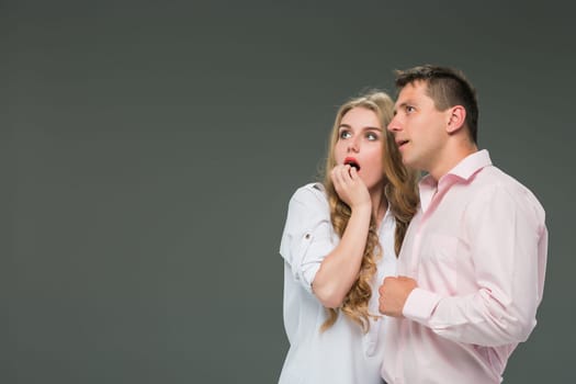 Portrait of a young surprised couple standing against gray studio background