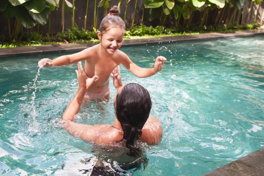 Happy family, active father with little child, adorable toddler girl, having fun together in outdoors swimming pool in water park during sunny summer sea vacation in tropical resort.