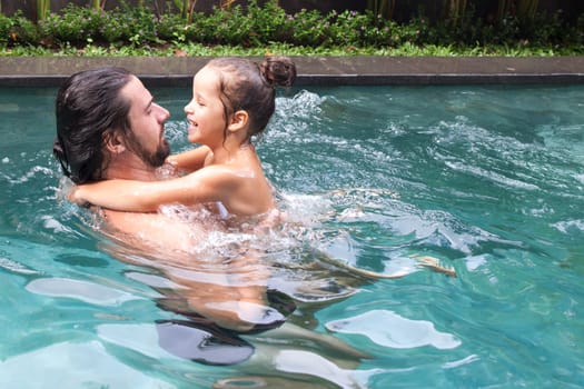 Happy family, active father with little child, adorable toddler girl, having fun together in outdoors swimming pool in water park during sunny summer sea vacation in tropical resort.