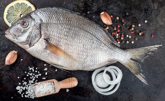 Above view of fresh uncooked dorado fish with various condiments over black pan