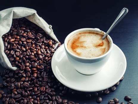 Fresh delicious coffee. Photo of coffee cup and coffee beans scattered from a canvas bag.
