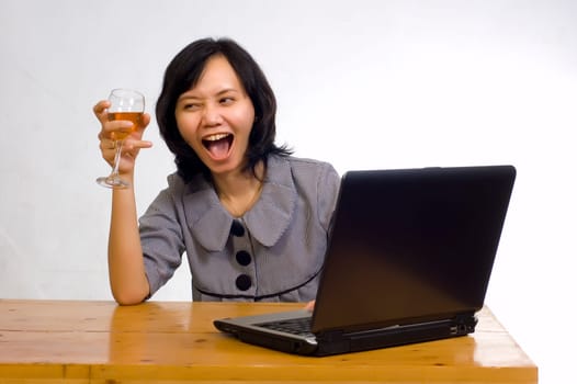 Beautiful asian business woman celebrating her success with wine in front of her computer